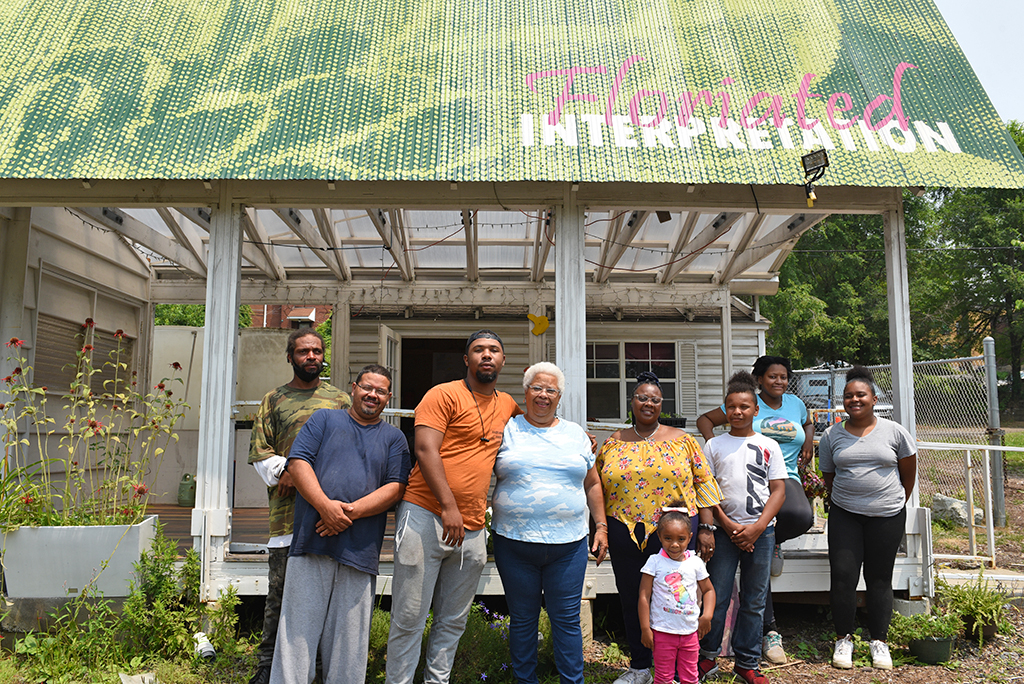 A group stands in front of a storefront that reads Floriated Interpretation