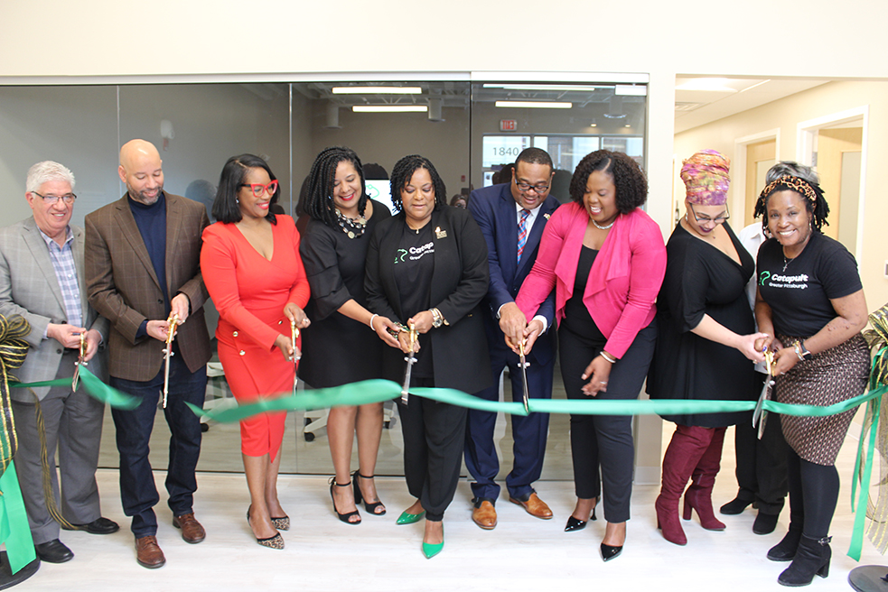 Event attendees and partners gather around a green ribbon for a ceremonial ribbon cutting