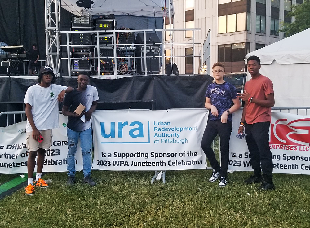 Image shows young boys in front of URA Sponsorship sign at 2023 Juneteenth event.