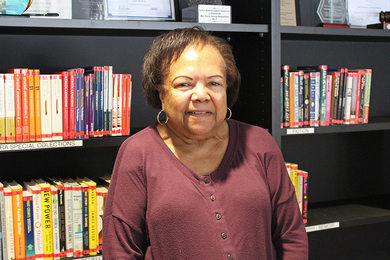 Pam Brown smiling in front of a bookshelf in the office library