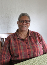 Homeowner Assistant Program client and Carrick homeowner Shirley Roberts sits at her dining room table and smiles.